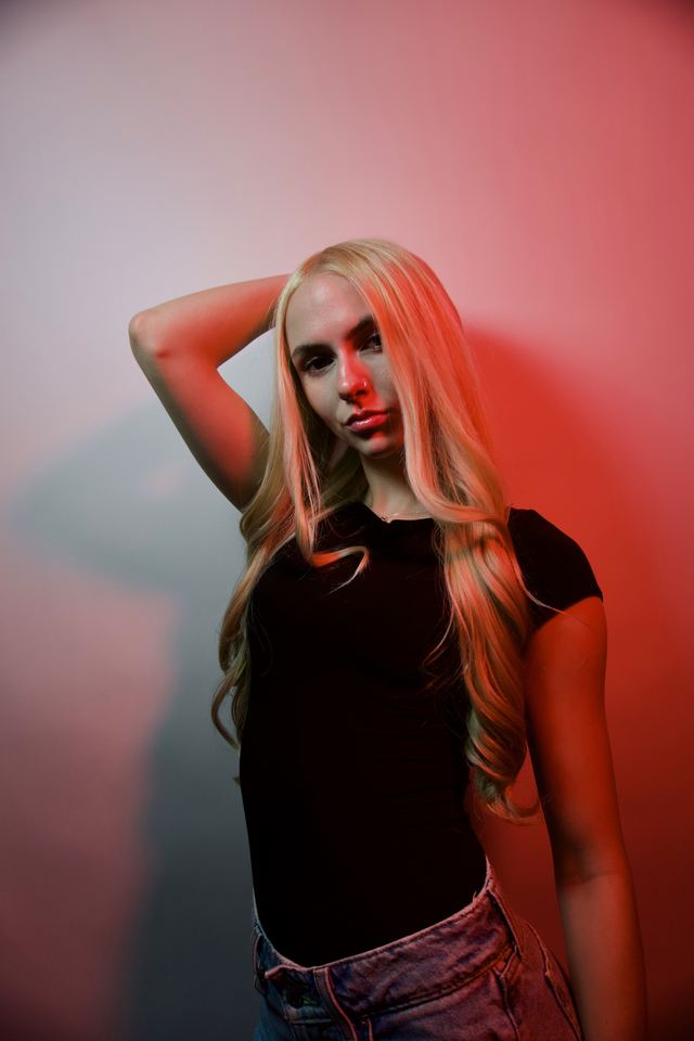 Bethany posing with one arm raised under red studio light